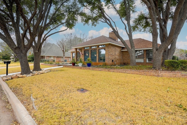 view of front of property featuring brick siding, a chimney, and a front lawn