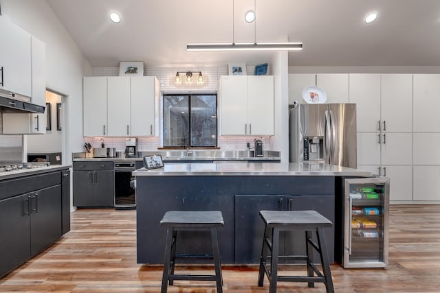 kitchen with wine cooler, a breakfast bar area, stainless steel appliances, light countertops, and a kitchen island