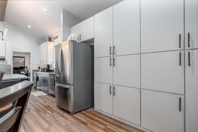 kitchen with light wood finished floors, white cabinetry, appliances with stainless steel finishes, and vaulted ceiling