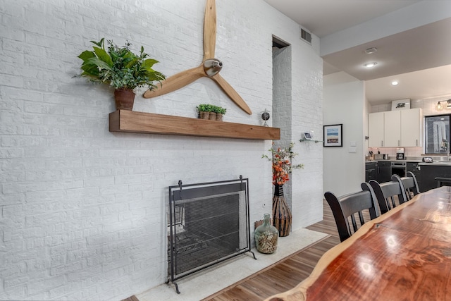 dining space with a fireplace with flush hearth, visible vents, light wood-style flooring, and brick wall