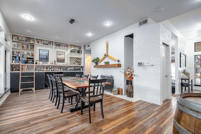 dining area featuring a brick fireplace, visible vents, and wood finished floors