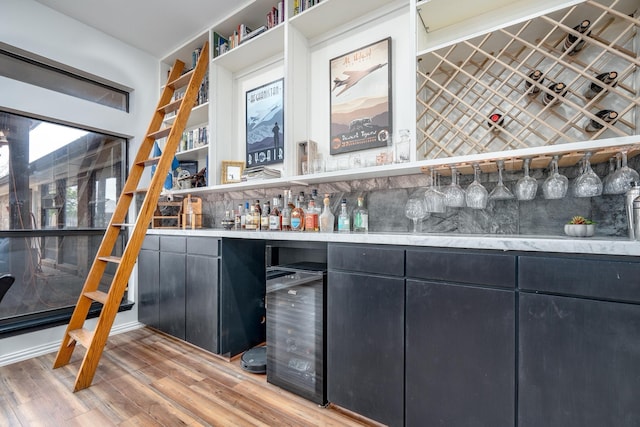 bar with a dry bar, light wood-style floors, beverage cooler, and decorative backsplash