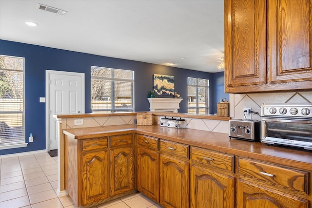 kitchen with light tile patterned floors, a peninsula, brown cabinetry, and visible vents