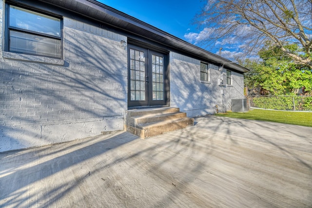 entrance to property featuring brick siding, fence, cooling unit, and french doors