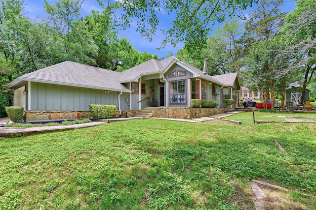 view of front facade with an attached garage, a shingled roof, stone siding, a front lawn, and board and batten siding