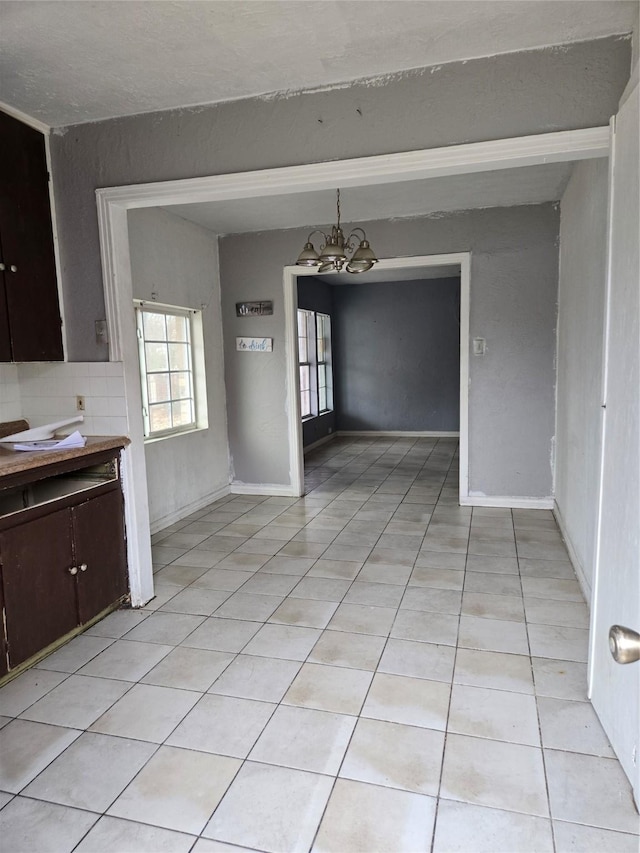 unfurnished dining area with light tile patterned floors, beamed ceiling, baseboards, and a notable chandelier