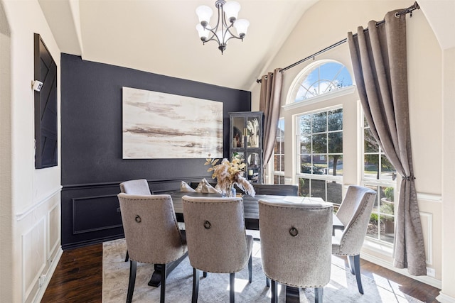 dining space with lofted ceiling, a decorative wall, wainscoting, wood finished floors, and a chandelier