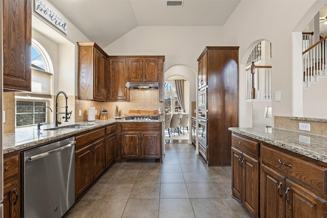 kitchen with light stone counters, vaulted ceiling, stainless steel appliances, under cabinet range hood, and a sink