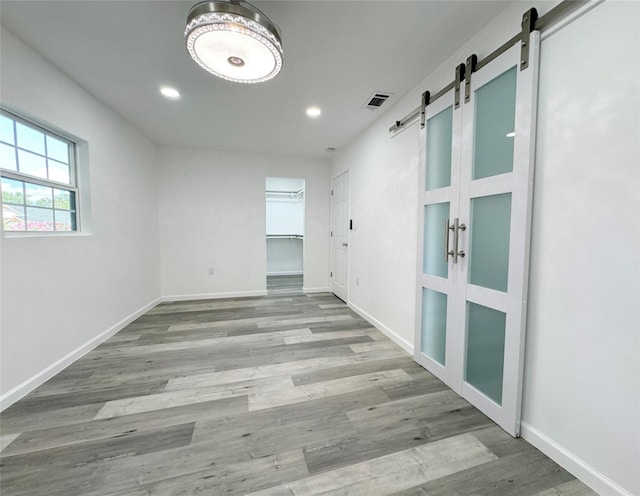 unfurnished room with a barn door, visible vents, baseboards, light wood-type flooring, and recessed lighting