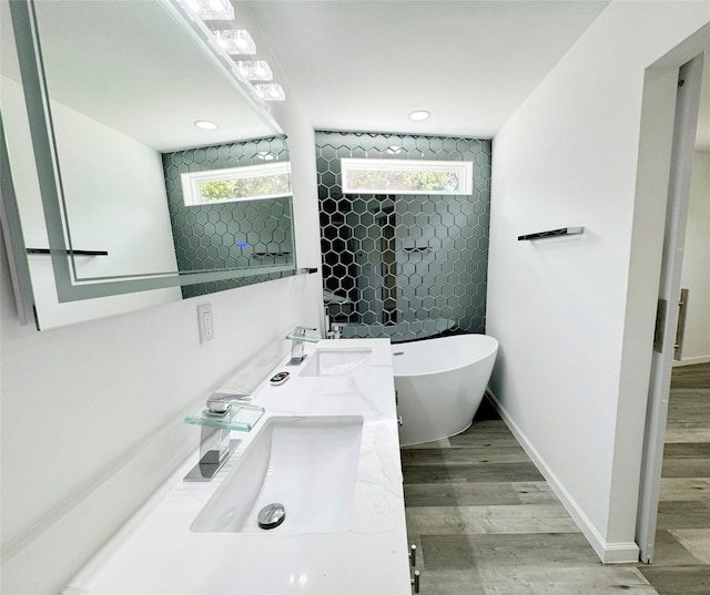 bathroom featuring wood finished floors, a freestanding tub, a sink, and baseboards