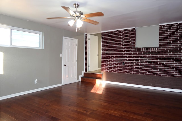 spare room featuring a ceiling fan, brick wall, baseboards, and wood finished floors