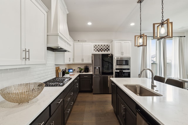 kitchen with custom range hood, appliances with stainless steel finishes, decorative light fixtures, white cabinetry, and a sink