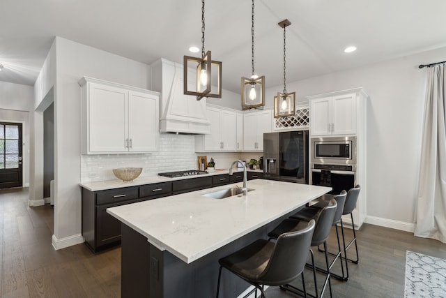 kitchen featuring premium range hood, a kitchen island with sink, white cabinets, and a sink