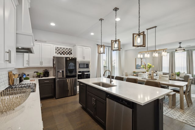 kitchen featuring hanging light fixtures, appliances with stainless steel finishes, open floor plan, white cabinetry, and a sink