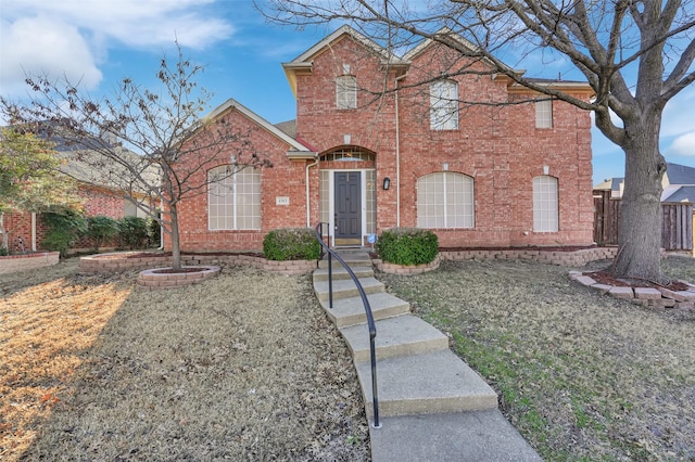 traditional home with brick siding, a front lawn, and fence