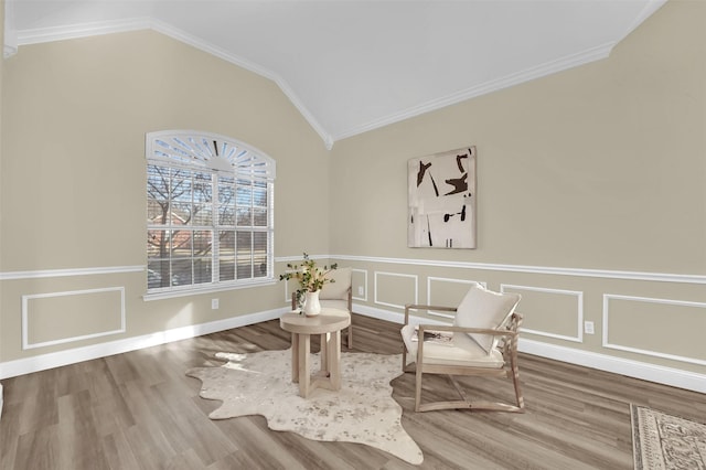 sitting room with crown molding, vaulted ceiling, a decorative wall, and wood finished floors