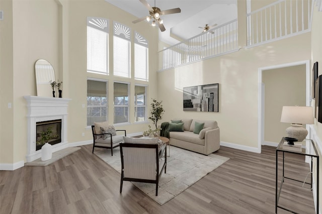 living room featuring light wood-type flooring, ceiling fan, baseboards, and a glass covered fireplace