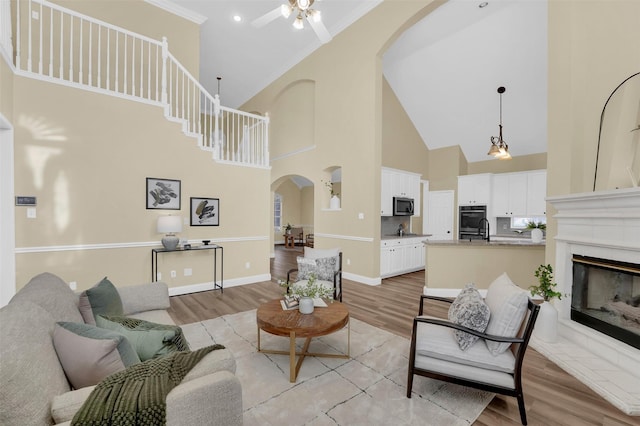 living room with arched walkways, ornamental molding, light wood-type flooring, and a glass covered fireplace