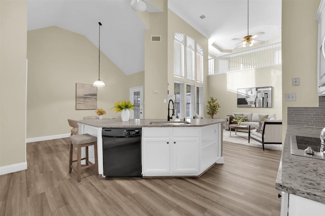 kitchen with a sink, white cabinetry, open floor plan, and light stone counters