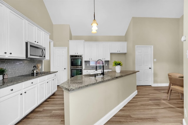 kitchen with stainless steel appliances, a sink, white cabinets, hanging light fixtures, and an island with sink