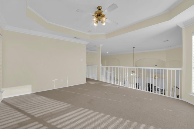 empty room with a ceiling fan, a raised ceiling, carpet flooring, and crown molding