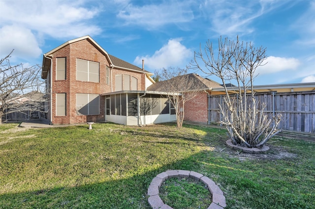 back of house featuring brick siding, a lawn, fence, and a sunroom