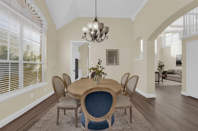 dining room featuring an inviting chandelier, arched walkways, vaulted ceiling, and wood finished floors