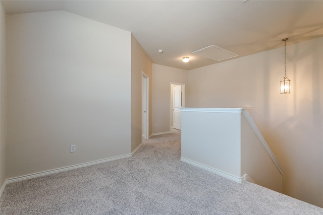 empty room with light carpet, attic access, baseboards, and vaulted ceiling