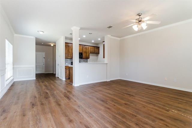 unfurnished living room featuring ornamental molding, dark wood-type flooring, decorative columns, and a ceiling fan