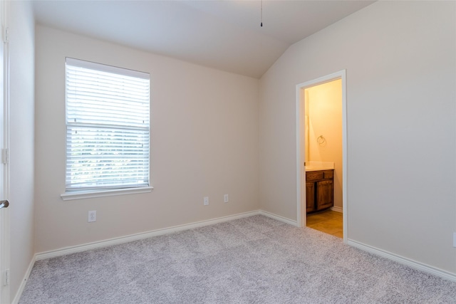 unfurnished bedroom featuring lofted ceiling, ensuite bath, baseboards, and light colored carpet