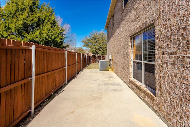 view of side of property with fence private yard, brick siding, a patio, and central air condition unit