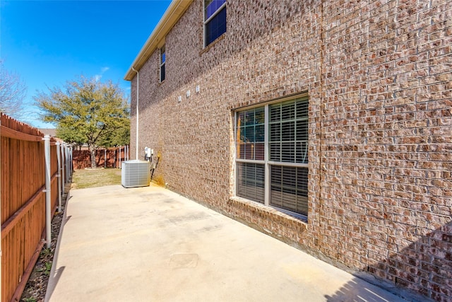 view of property exterior featuring central air condition unit, brick siding, a fenced backyard, and a patio