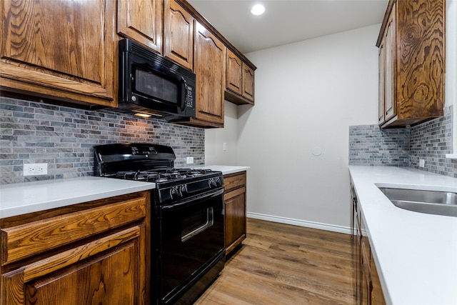 kitchen with baseboards, light countertops, black appliances, and wood finished floors