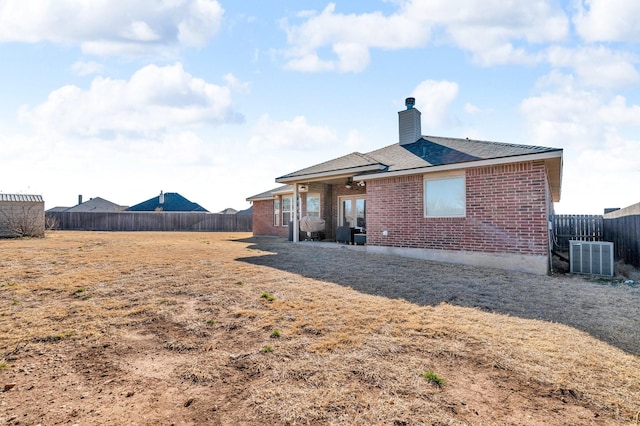 back of house with a fenced backyard, a chimney, cooling unit, and brick siding