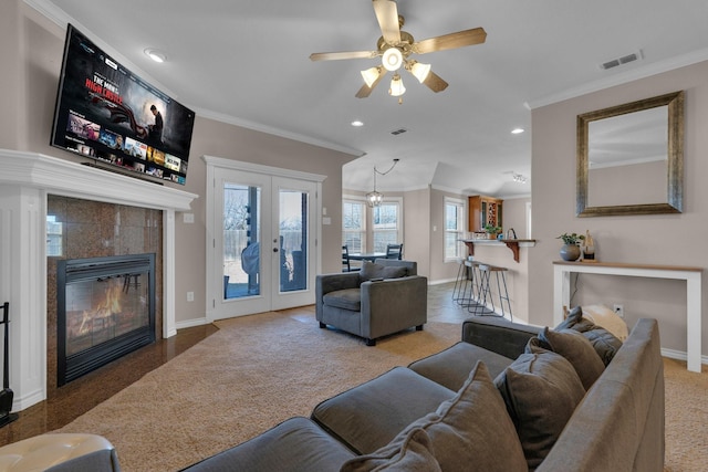 carpeted living area with visible vents, baseboards, french doors, ornamental molding, and a tiled fireplace