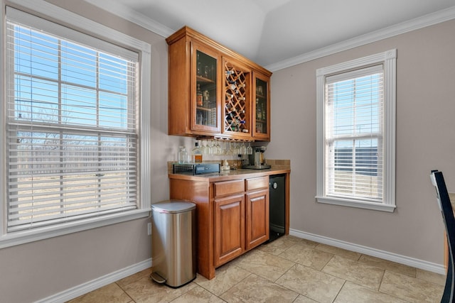 bar featuring a bar, baseboards, crown molding, and lofted ceiling