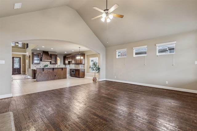 unfurnished living room featuring arched walkways, high vaulted ceiling, ceiling fan, and light wood-style floors