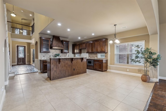 kitchen with custom range hood, glass insert cabinets, stainless steel microwave, a kitchen breakfast bar, and light countertops