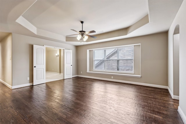 unfurnished bedroom with a tray ceiling, dark wood-style flooring, visible vents, a ceiling fan, and baseboards