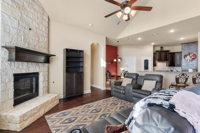 living area featuring a stone fireplace, dark wood-style flooring, visible vents, and a ceiling fan