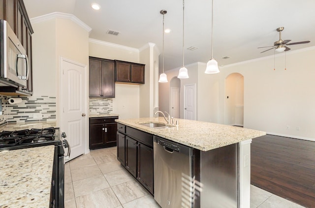 kitchen featuring arched walkways, pendant lighting, appliances with stainless steel finishes, a kitchen island with sink, and a sink