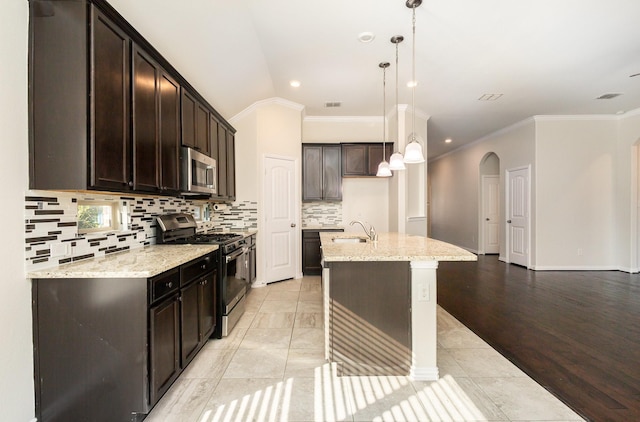 kitchen with appliances with stainless steel finishes, a center island with sink, hanging light fixtures, and light stone counters