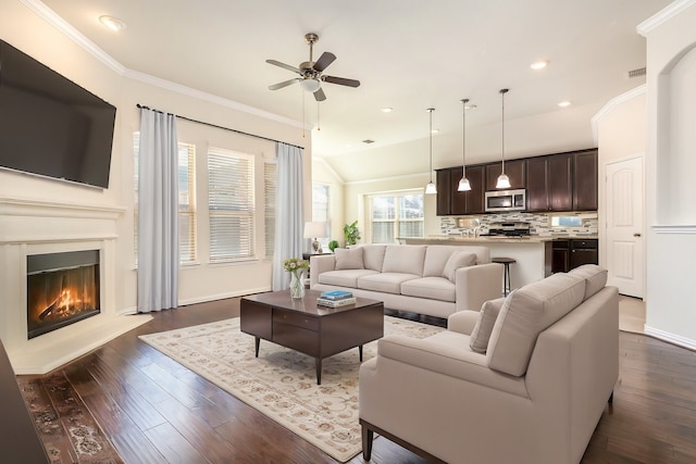 living room with ornamental molding, a glass covered fireplace, dark wood-style flooring, and a ceiling fan