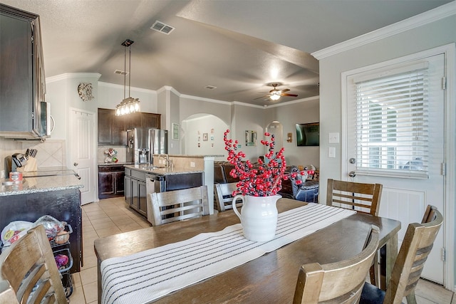 dining area with light tile patterned floors, visible vents, arched walkways, ceiling fan, and ornamental molding