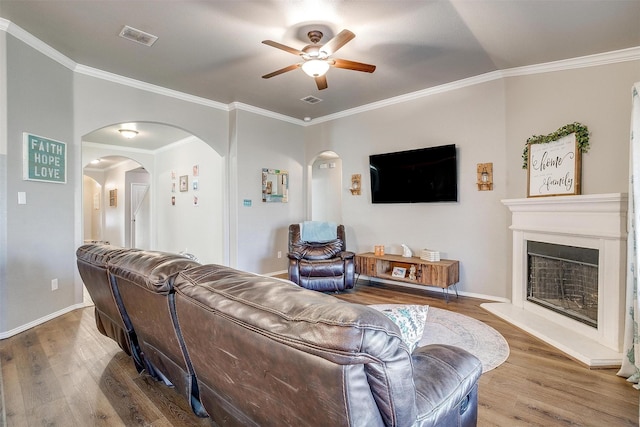 living area featuring arched walkways, visible vents, a fireplace with raised hearth, and wood finished floors