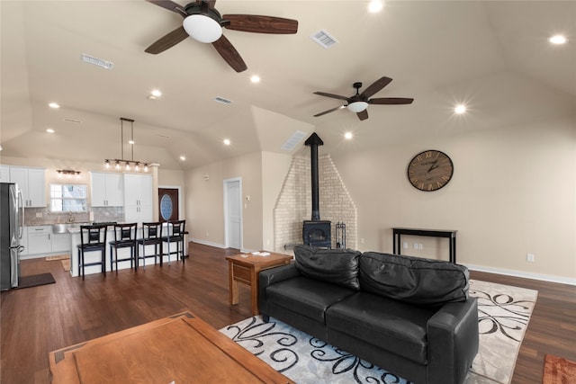 living area featuring dark wood-type flooring, lofted ceiling, a wood stove, and visible vents