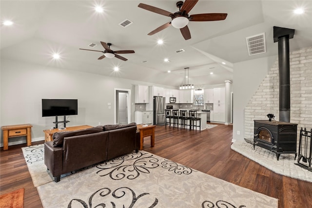 living room featuring lofted ceiling, a wood stove, visible vents, and wood finished floors