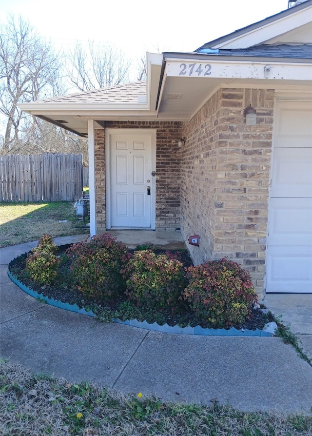 property entrance with a garage, brick siding, and fence