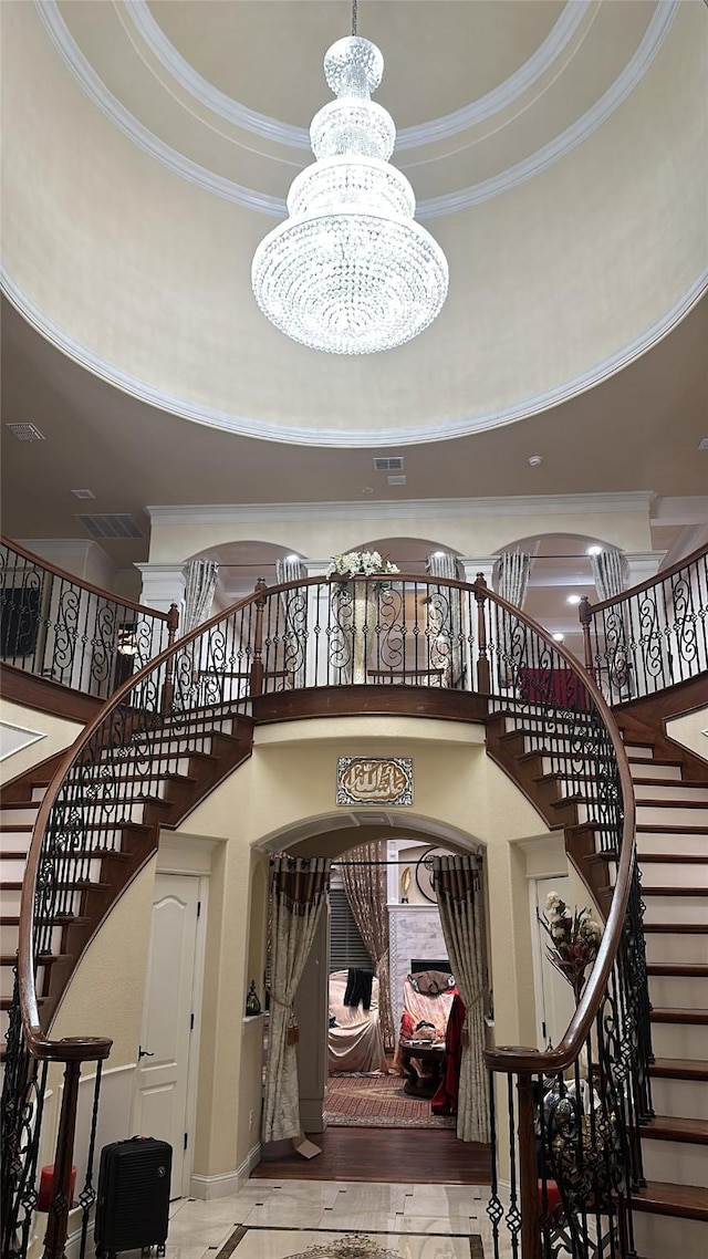 stairway featuring crown molding, a raised ceiling, a chandelier, and a towering ceiling