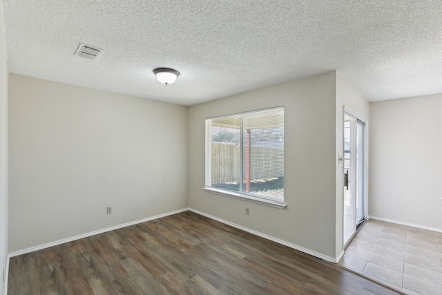 empty room with a textured ceiling, wood finished floors, visible vents, and baseboards